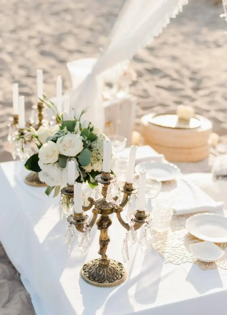 An elegant beachside table setup with flowers and candle holders, perfect for a romantic occasion.